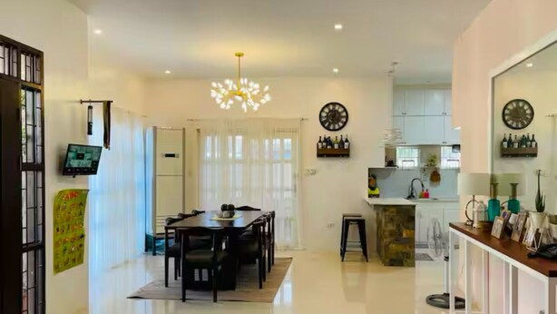 A modern kitchen with white cabinets, a dining area with a table and chairs, and a large window with curtains. - 5BR House with Centralized AC, Backyard & Office (Roxas City)