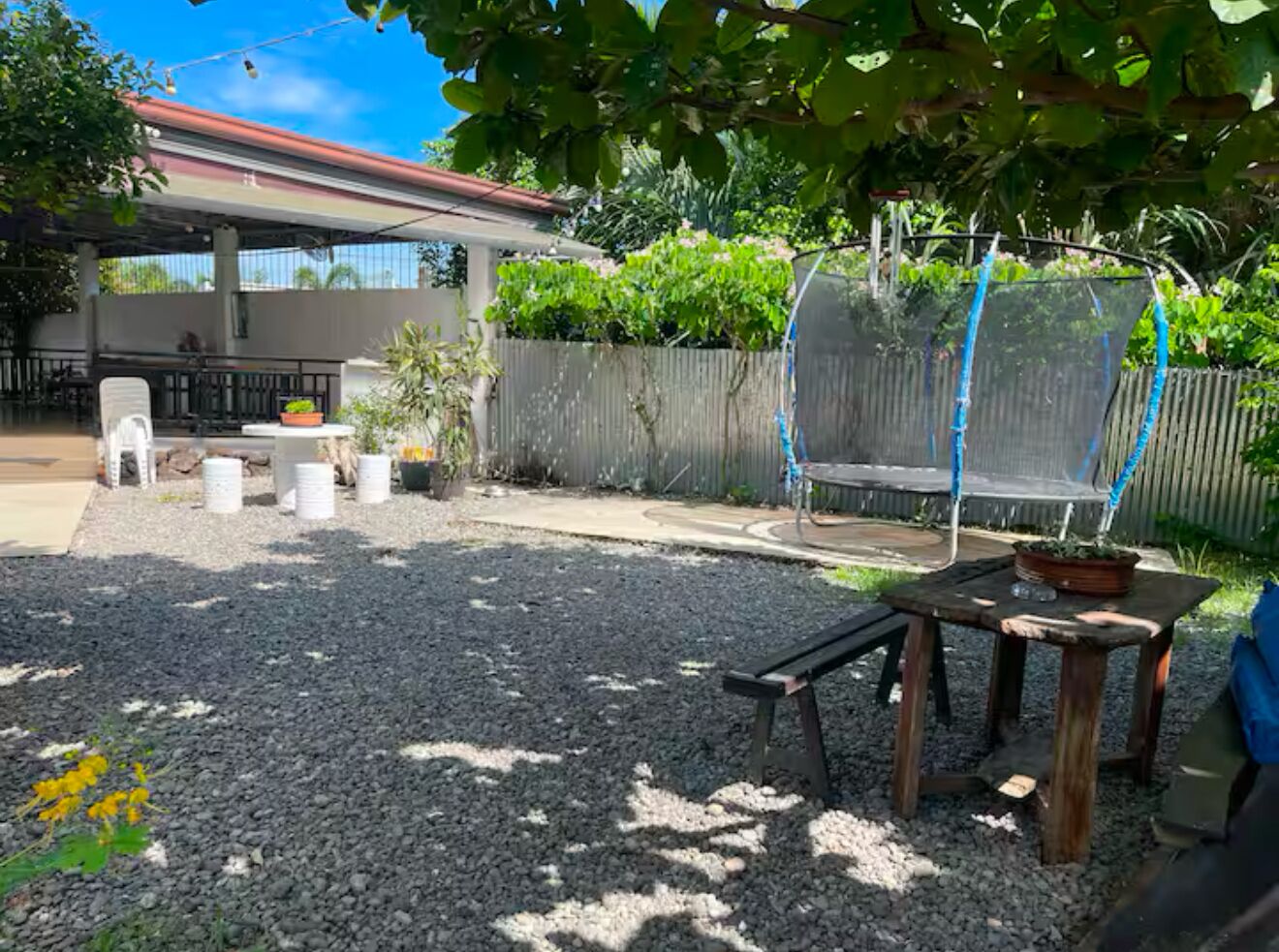 A backyard with a covered patio, a trampoline, and a garden area with potted plants.