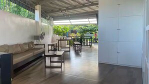 A spacious room with a wooden floor, a sofa, a dining table, and chairs. There is a white cabinet and a ceiling fan. - 5BR House with Centralized AC, Backyard & Office (Roxas City)
