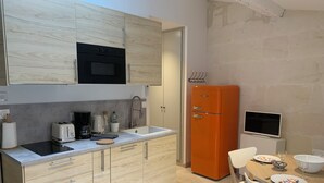 A modern kitchen with wooden cabinets, a built-in oven, a sink, and a dining area with a table and chairs. - Holiday in Arles: Appartement de l'Amphithéâtre C (Arles)