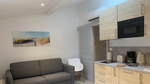 A modern kitchen with a grey sofa, a dining table, and a painting of a beach scene. - Holiday in Arles: Appartement de l'Amphithéâtre C (Arles)