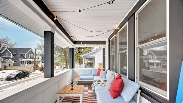 A covered porch with a sofa and a coffee table, large windows, and a view of the street.