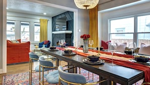 A modern dining area with a long table set for a meal, a chandelier, and a view of the outdoors.