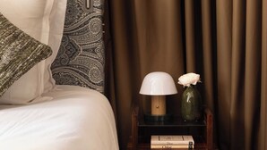 A neatly made bed with patterned pillows, a bedside table with a lamp and books, and a hanging light fixture.