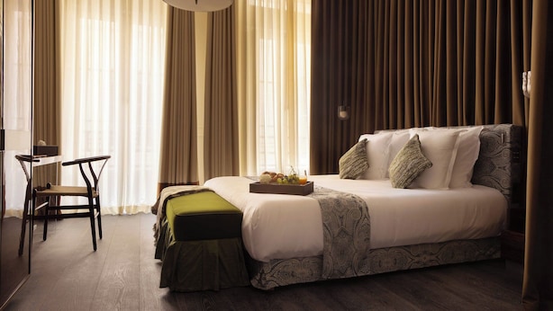 A hotel room with a bed, a desk, and a chair. There is a tray with fruits on the bed.