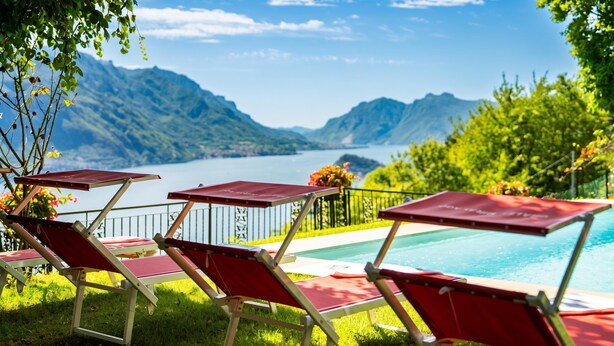 A poolside area with red lounge chairs and a view of mountains and a lake.