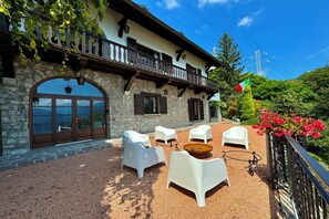 A stone building with a balcony, outdoor seating, and a flag.