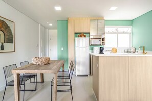 A modern kitchen with a wooden island, a refrigerator, and a microwave. There is a dining area with a table and chairs. - Casa Tiwa: Stunning  Flat in Perfect Location in Florianópolis (Lagoa da Conceição Florianópolis)