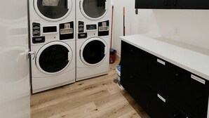 A laundry room with four stacked washing machines, a black cabinet, and a white countertop. - The Charlotte • King Bed • Downtown Woodstock (Woodstock)