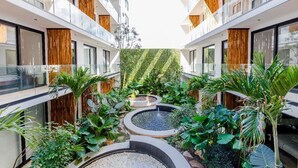 Un patio de hotel moderno con varios balcones, abundante vegetación y una fuente central.