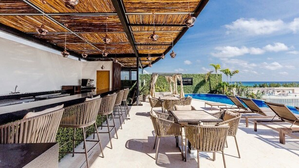 Un bar en la azotea con mobiliario de mimbre, una piscina y vistas al océano.
