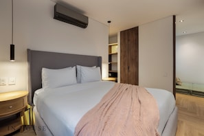 A modern bedroom with a large bed, bedside tables, a wooden wardrobe, and built-in shelving.