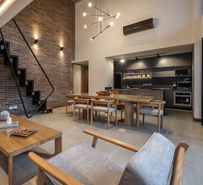 A modern kitchen with built-in appliances, a dining area with a wooden table and chairs, and a staircase with exposed brick walls.
