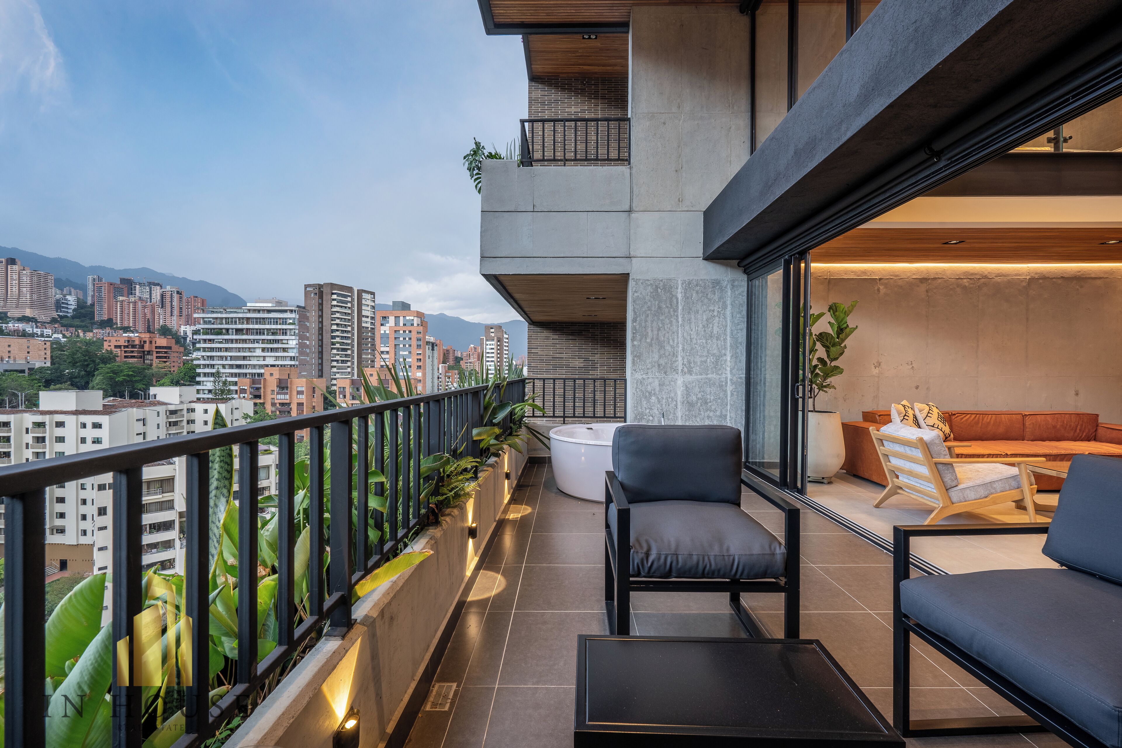A modern balcony with a view of a cityscape, featuring a sofa, a coffee table, and potted plants.