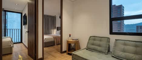 A modern hotel room with a large window, a sofa, a bed, and a small table with a vase.