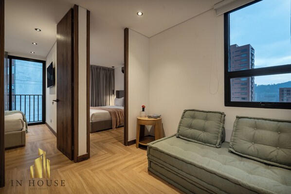 A modern hotel room with a large window, a sofa, a bed, and a small table with a vase.