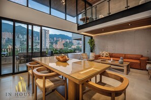 Een moderne woonkamer met een glazen eettafel, houten stoelen, een leren bank en uitzicht op de stad.
