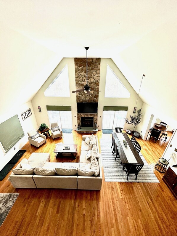 A spacious loft with a high ceiling, a stone fireplace, a dining area with a long table, and a cozy seating area with a sofa.
