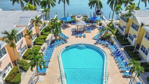 Ein großer Swimmingpool, umgeben von Liegestühlen und Sonnenschirmen, mit Palmen und Blick auf das Wasser.