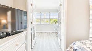 Ein Schlafzimmer mit Fernseher auf einer Kommode, einem Fenster mit Jalousien und einem Bett mit gemustertem Überwurf.