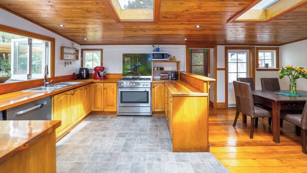 A modern kitchen with wooden cabinets, a central island, and a dining area with a table and chairs.