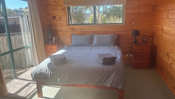 Une chambre à coucher dans une cabane en bois, avec un lit, deux tables de chevet, une fenêtre et une vue sur l’extérieur.