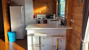 Une cuisine de taille réduite avec des murs en bois, un réfrigérateur blanc, une cuisinière et deux tabourets de bar.
