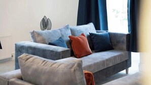 A modern living room with a grey sofa, multiple cushions, a decorative wall piece, and a window with curtains.