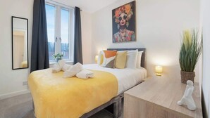A hotel room with a bed, bedside table, lamp, and a painting on the wall.