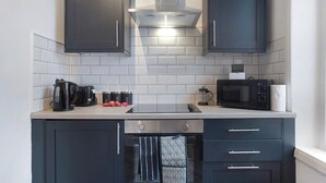 A modern kitchen with dark cabinets, a stainless steel range hood, a microwave, and a kettle on the countertop.