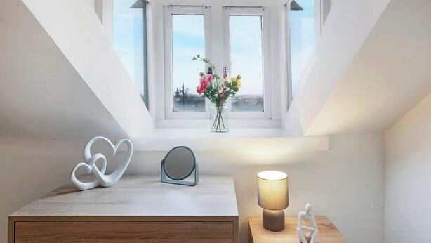A room with a skylight, a bedside table with a lamp, a vase with flowers, and a heart-shaped decoration.