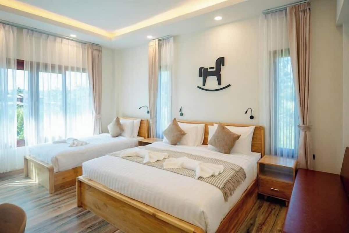 Ein Hotelzimmer mit zwei Betten, Holzboden, einem großen Fenster mit Vorhängen und einer Wandleuchte.
