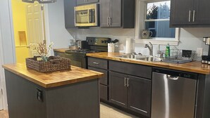 A modern kitchen with dark cabinetry, a wooden countertop, a stainless steel dishwasher, and a microwave.