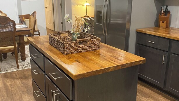 A kitchen with a central island, dark cabinets, a refrigerator, and a dining area with chairs and a table.