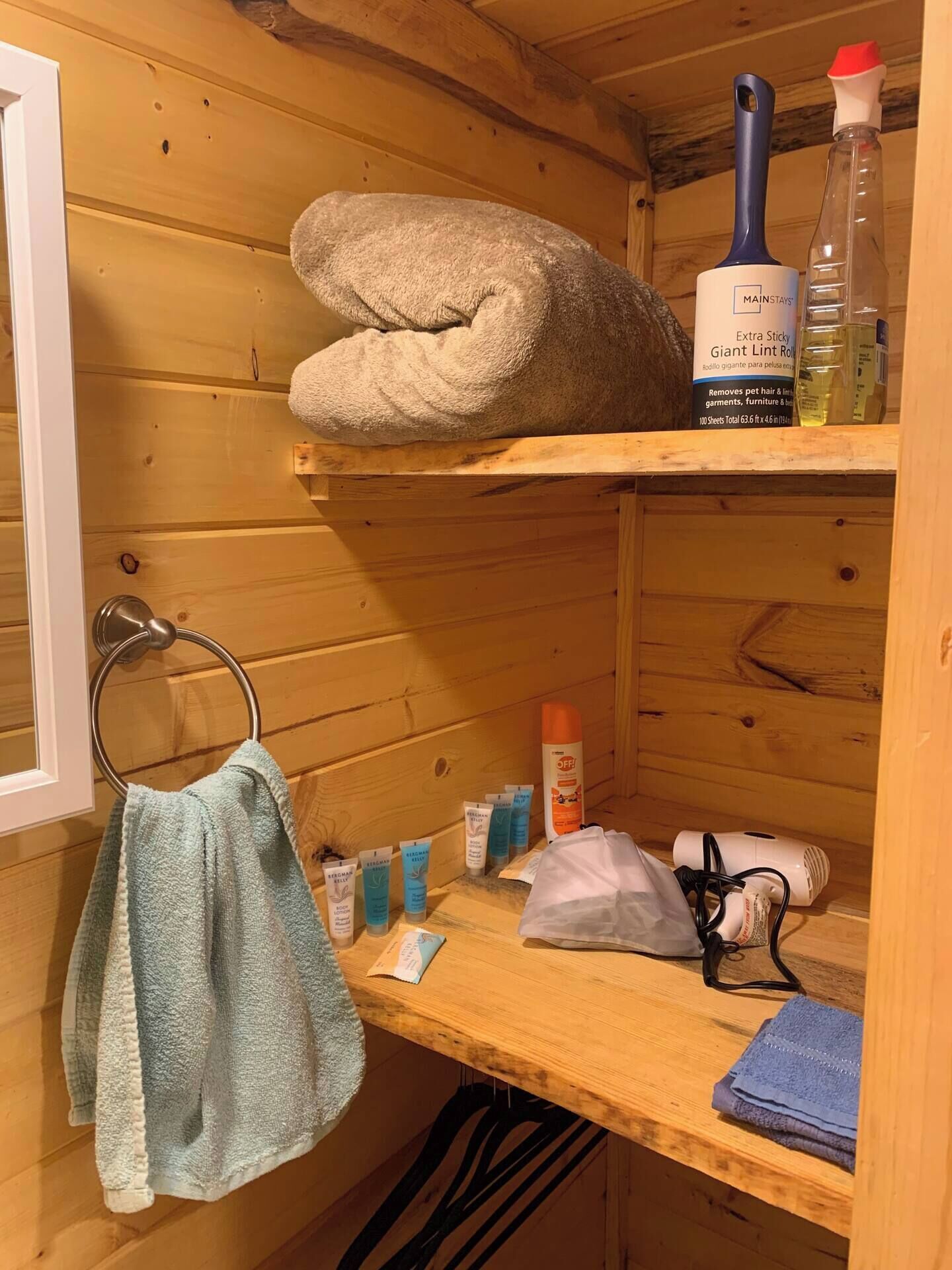 Interior de una cabaña de madera con un perchero, un estante con productos de limpieza y una toalla doblada.