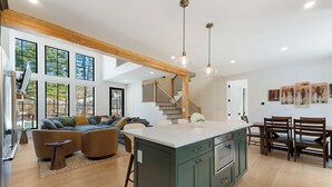 A spacious living area with a large island, a staircase, and a dining area with wooden chairs and a table. - Luxury Mountain Escape (North Conway)