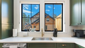 A kitchen with a large window, stainless steel sink, and green cabinets. - Luxury Mountain Escape (North Conway)