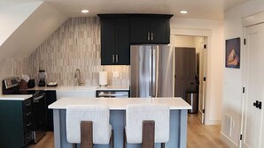 Una cocina moderna con una isla central, armarios oscuros y electrodomésticos de acero inoxidable.