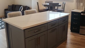 Una cocina moderna con una isla grande, armarios oscuros y un comedor con mesa y sillas.
