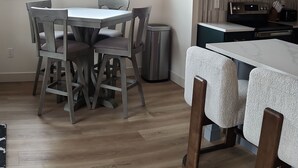 Una cocina moderna con horno y microondas integrados, una zona de comedor con mesa y sillas de madera, y un ventanal con vistas a un paisaje nevado.