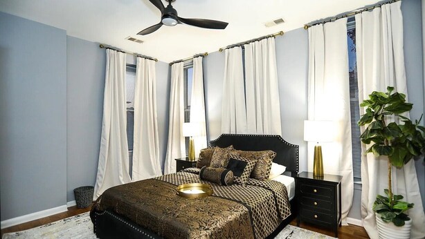 Une chambre à coucher avec un lit, des tables de chevet, un ventilateur de plafond et des rideaux.