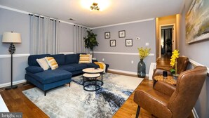 Un salon moderne avec un canapé bleu, une table basse ronde et un fauteuil en cuir marron. Un grand tableau orne le mur et une plante est posée sur le sol.