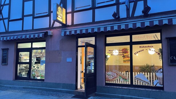 Un bistró con un amplio ventanal que muestra alimentos y un cartel que indica servicio para llevar.