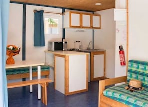 A compact kitchenette with a microwave, coffee maker, and sink. There is a bench and a plaid sofa with a straw hat on it.