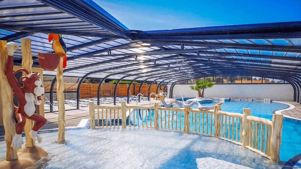 An indoor swimming pool with a glass ceiling, wooden deck, and a monkey sculpture.
