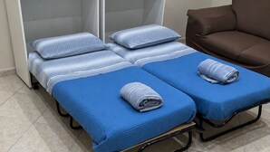 Une chambre avec deux lits, chacun agrémenté de draps et d’oreillers bleus, un canapé marron et une armoire blanche.