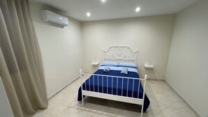 Une chambre à coucher avec un lit, des rideaux, un appareil de climatisation et un sol carrelé.