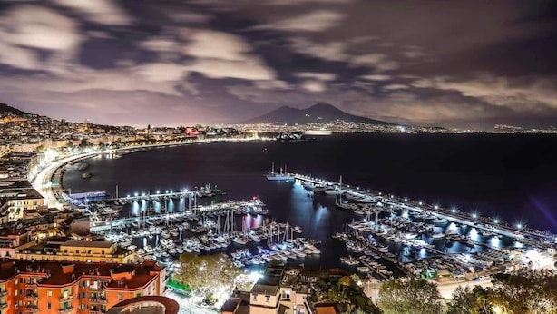 Un port de plaisance où sont amarrés de nombreux bateaux, une vue sur la ville en arrière-plan et une montagne illuminée.