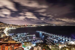 A marina with numerous boats docked, a cityscape in the background, and a mountain with lights. - Naples' home in the historic center (Napoli)
