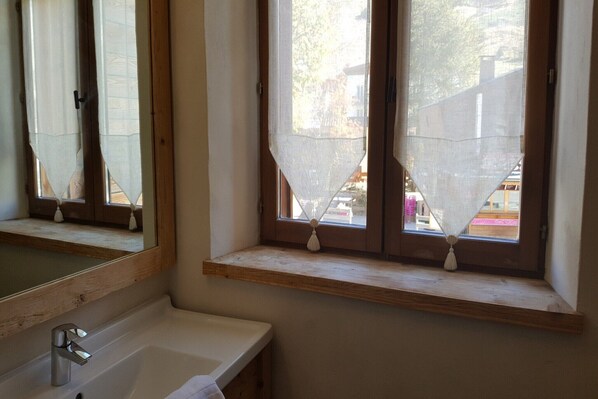 A bathroom with a wooden vanity, a mirror, and a window with a view of the outside.